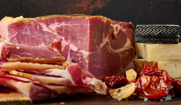 A piece of prosciutto, slices of ciabatta and cheese on a wooden board
