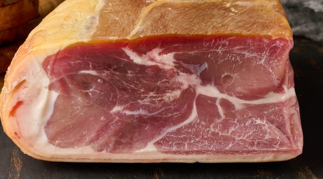 A piece of prosciutto on a wooden board, close up
