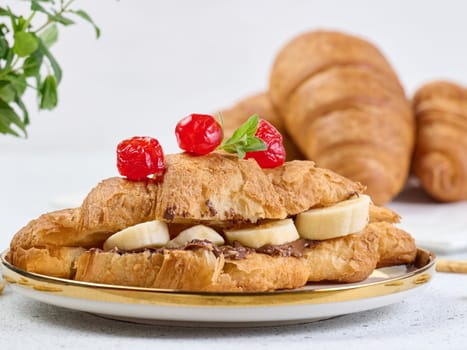 Croissant with chocolate spread and banana pieces in a white round plate on the table, breakfast