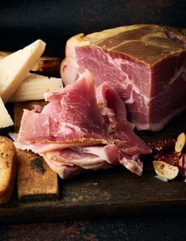 A piece of prosciutto, slices of ciabatta and cheese on a wooden board, close up