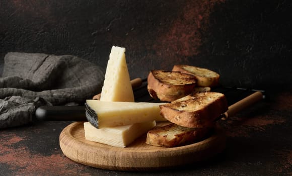 Triangular pieces of cheese and fried ciabatta slices on a wooden board