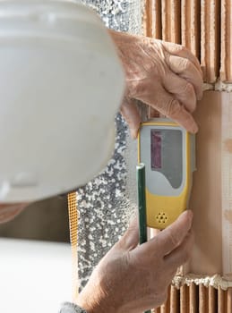 Craftsman in white helmet and grey dusty working clothing measuring with horizontal rotary laser level. Engineer during measurement work, construction or renovation site