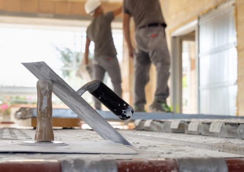 Two dusty caftsmen working to a ceiling inside a room standing on scaffoldings, back view. Men in grey work clothes and white helmets during construction or renovation process