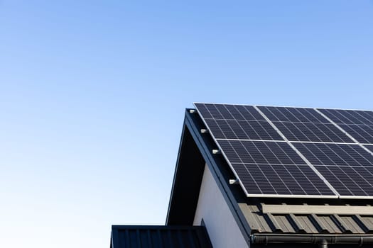 Modern house with solar panels stand-alone photovoltaic plant system on household metal sheet rooftop. Clear blue sky background. Clean alternative energy concept. Professional installation, go green