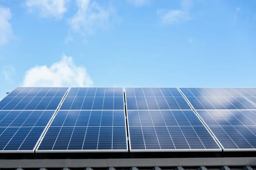 Solar panel cells on cloudy blue sky background. Clean alternative energy power concept. Modern house with solar panels stand-alone photovoltaic plant system on metal sheet roof. Go green