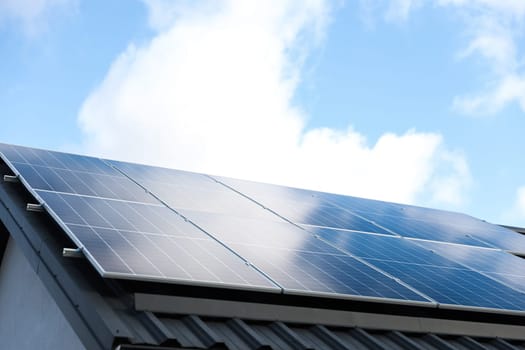 Solar panel cells on cloudy blue sky background. Clean alternative energy power concept. Modern house with solar panels stand-alone photovoltaic plant system on metal sheet roof. Go green