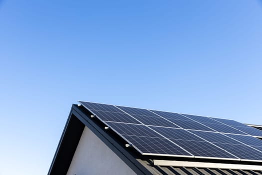 Modern house with solar panels stand-alone photovoltaic plant system on household metal sheet rooftop. Clear blue sky background. Clean alternative energy concept. Professional installation, go green
