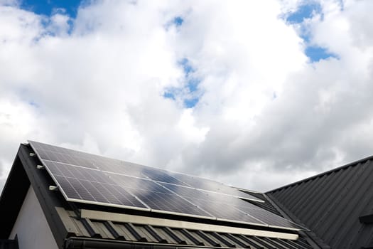 Clean alternative energy. Modern house with solar panels stand-alone photovoltaic plant system on household metal sheet rooftop. Clouds, blue sky background. Professional installation, go green