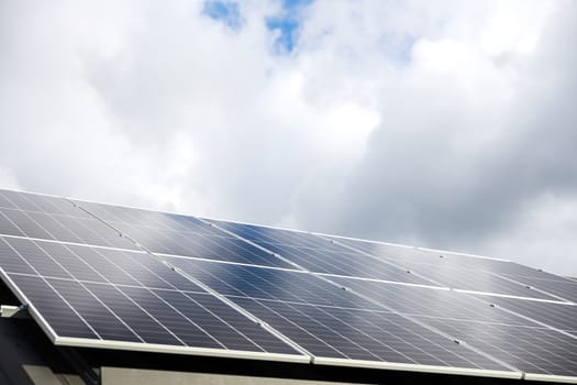 Aerial view of solar panel cells on clouds, blue sky background. Clean alternative energy power in nature concept, sustainable resources. House with solar panel photovoltaic plant system on metal roof