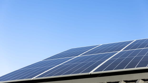 Aerial view of solar panel cells on clear blue sky background. Clean alternative energy power concept, sustainable resources. Modern house, solar panels stand-alone photovoltaic plant system on roof