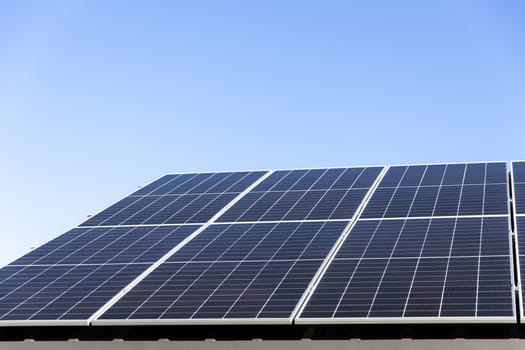 Aerial view of solar panel cells on clear blue sky background. Clean alternative energy power concept, sustainable resources. Modern house, solar panels stand-alone photovoltaic plant system on roof