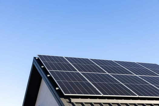 Modern house with solar panels stand-alone photovoltaic plant system on household metal sheet rooftop. Clear blue sky background. Clean alternative energy concept. Professional installation, go green