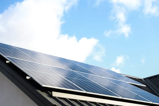 Solar panel cells on cloudy blue sky background. Clean alternative energy power concept. Modern house with solar panels stand-alone photovoltaic plant system on metal sheet roof. Go green