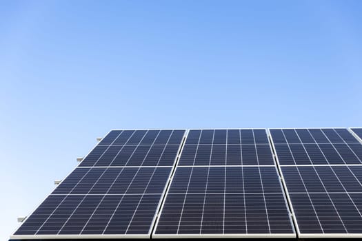 Aerial view of solar panel cells on clear blue sky background. Clean alternative energy power concept, sustainable resources. Modern house, solar panels stand-alone photovoltaic plant system on roof
