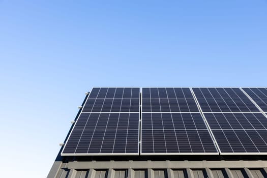 Modern house with solar panels stand-alone photovoltaic plant system on household metal sheet roof. Clear blue sky background. Clean alternative energy power concept, sustainable resources