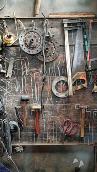 A cluttered workshop scene showcasing an assortment of tools hanging on a wooden wall and surrounding shelves, creating a rustic and industrial atmosphere.