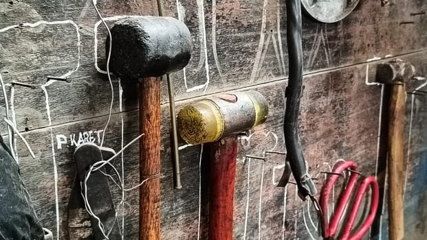 A cluttered workshop scene showcasing an assortment of tools hanging on a wooden wall and surrounding shelves, creating a rustic and industrial atmosphere.