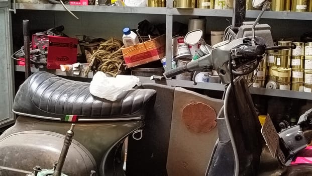 A classic scooter and various spare parts in an old workshop setting. The scene suggests machinery repair, vintage restoration, and mechanical work, symbolizing nostalgia and automotive passion.