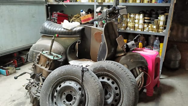 A classic scooter and various spare parts in an old workshop setting. The scene suggests machinery repair, vintage restoration, and mechanical work, symbolizing nostalgia and automotive passion.