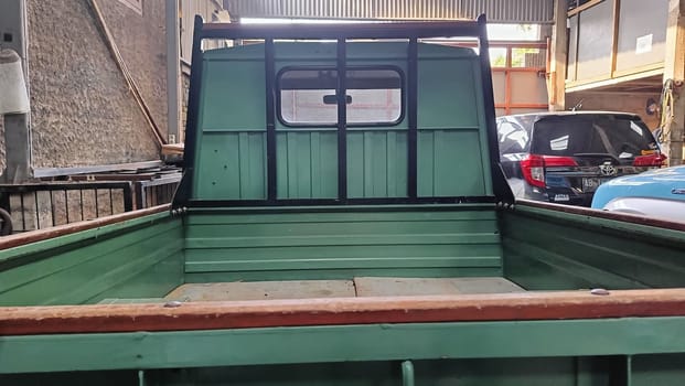 An empty green pickup truck bed inside an industrial garage featuring parked vehicles and storage. Captures the essence of vintage utility and automotive design.