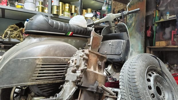A classic scooter and various spare parts in an old workshop setting. The scene suggests machinery repair, vintage restoration, and mechanical work, symbolizing nostalgia and automotive passion.