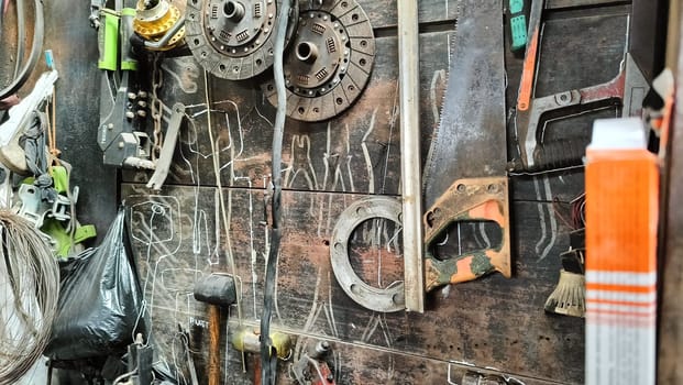 A cluttered workshop scene showcasing an assortment of tools hanging on a wooden wall and surrounding shelves, creating a rustic and industrial atmosphere.