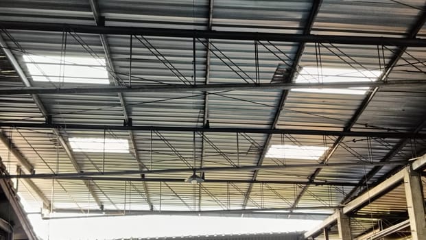 View of a sturdy metal roof with beams inside a spacious warehouse. The structure depicts industrial architecture, showcasing strength and functionality. This space is ideal for storage and manufacturing.