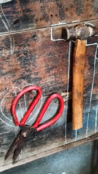 A cluttered workshop scene showcasing an assortment of tools hanging on a wooden wall and surrounding shelves, creating a rustic and industrial atmosphere.
