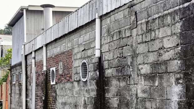 An industrial building partially hidden by a brick wall under a blue sky. The image captures urban architecture with a mix of materials and textures in a relaxed setting.