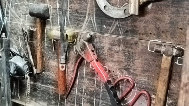 A cluttered workshop scene showcasing an assortment of tools hanging on a wooden wall and surrounding shelves, creating a rustic and industrial atmosphere.