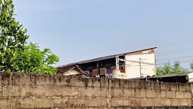 An industrial building partially hidden by a brick wall under a blue sky. The image captures urban architecture with a mix of materials and textures in a relaxed setting.