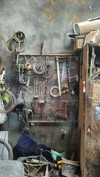 A cluttered workshop scene showcasing an assortment of tools hanging on a wooden wall and surrounding shelves, creating a rustic and industrial atmosphere.