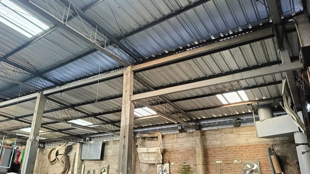 View of a sturdy metal roof with beams inside a spacious warehouse. The structure depicts industrial architecture, showcasing strength and functionality. This space is ideal for storage and manufacturing.