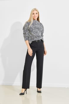 A model stands confidently in a chic black and white outfit, featuring a printed top and tailored pants, against a bright indoor backdrop, showcasing the latest fashion trends for a look book