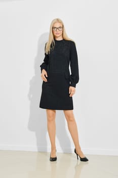 A model stands confidently in a contemporary indoor setting, showcasing a casual black dress paired with high heels. The well-lit space enhances the outfit's elegant details and modern design.