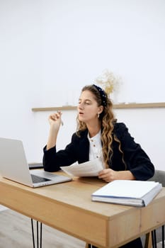 A young woman with long hair thoughtfully examines documents while seated at a modern desk. She appears focused, contemplating ideas. The bright office setup fosters a creative atmosphere.