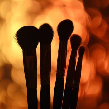 Dramatic silhouette of makeup brushes against a radiant background.