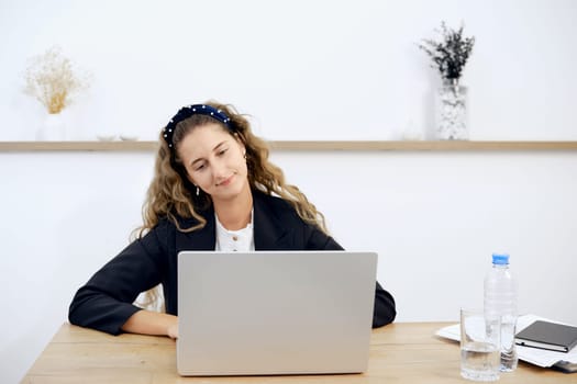 A focused woman with curly hair sits at a desk, engaged with her laptop. The workspace is minimal, with a bottle of water and notebook nearby, creating a productive and calm atmosphere.