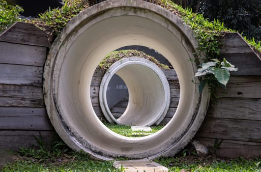 Bangkok, Thailand - Feb 19, 2025 - Park concrete tunnel made for Children's play as a rabbit, ducking through its numerous burrows. Outdoor playground with The kid's playing tunnel with Grass mound on top in the park for children, use it as your Space for text, Design, Wallpaper and Poster, Selective focus.