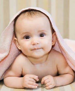 A cute baby lies peacefully on a soft surface, wrapped in a cozy pink towel, looking cheerful and content