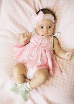 A charming baby girl, dressed in a lovely pink outfit, is comfortably resting on a cozy blanket with a pattern