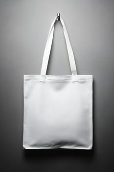 A plain white tote bag is suspended from a hook against a neutral background, showcasing its minimalist design and versatility for use.