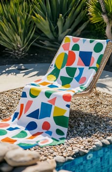 A vibrant poolside lounge chair adorned with a geometric patterned towel invites relaxation under the sun in a lush setting.