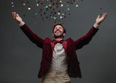 A man in a red blazer joyfully raises his arms while colorful confetti falls around him, creating a festive atmosphere.