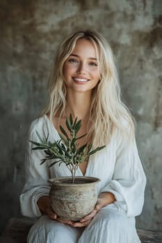 A woman with long hair smiles brightly while holding a small potted plant, creating a warm and inviting atmosphere indoors.