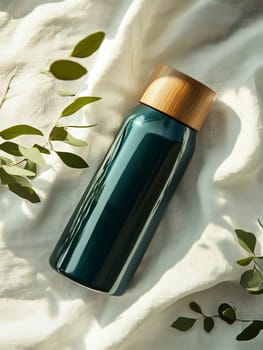 A sleek green water bottle with a bamboo lid rests on a light fabric, surrounded by green leaves, creating a serene atmosphere.