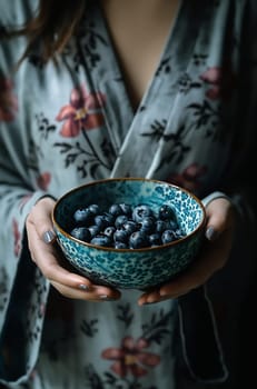 A person in a floral robe presents a beautifully patterned bowl filled with fresh blueberries, showcasing simple elegance.