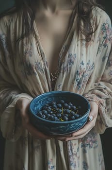 A woman in a floral-patterned robe holds a blue bowl filled with fresh blueberries, showcasing a cozy and serene atmosphere.