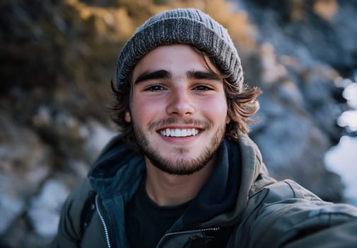 A young man with a friendly smile poses near rocky coastal terrain, showcasing his casual winter attire against a scenic background.