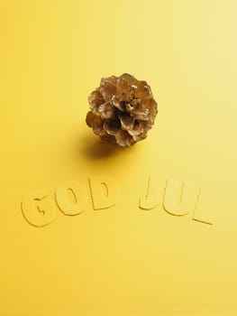 Yellow Christmas decoration with golden pine cone and the Scandinavian words God Jul, Scandinavian Merry Christmas
